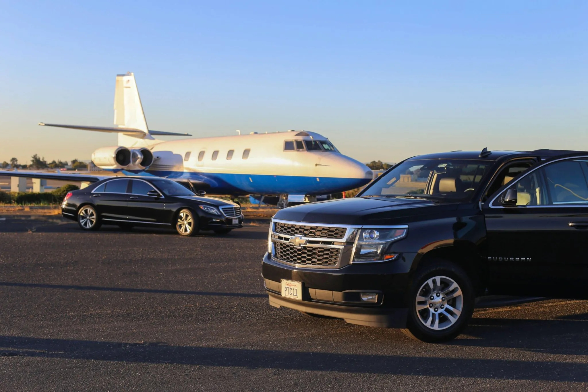 Luxury limousine and SUV parked beside a private jet on a runway, showcasing premium transportation services.